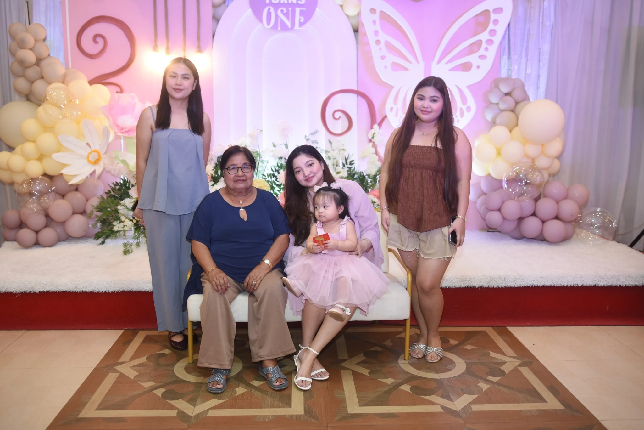 A small group poses around the seated birthday child against the pink floral backdrop.