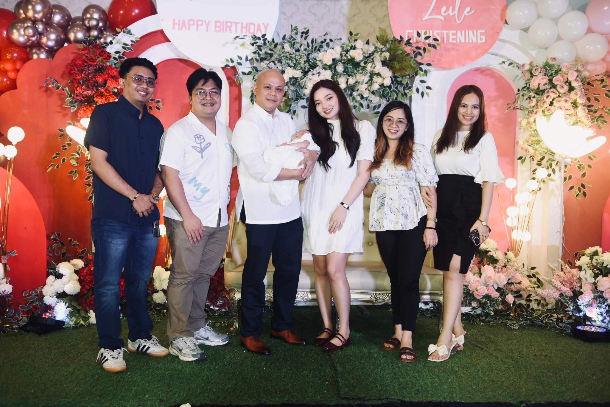 Guests gather around the baby for a portrait in front of the floral backdrop.