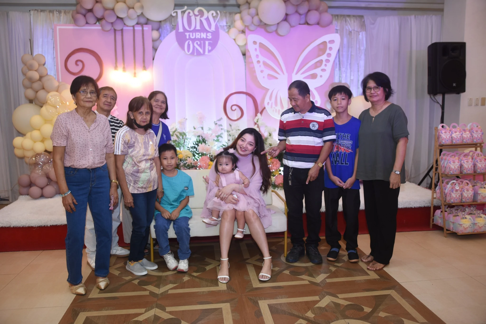 Guests and children stand around the birthday child for a portrait near the party favors.