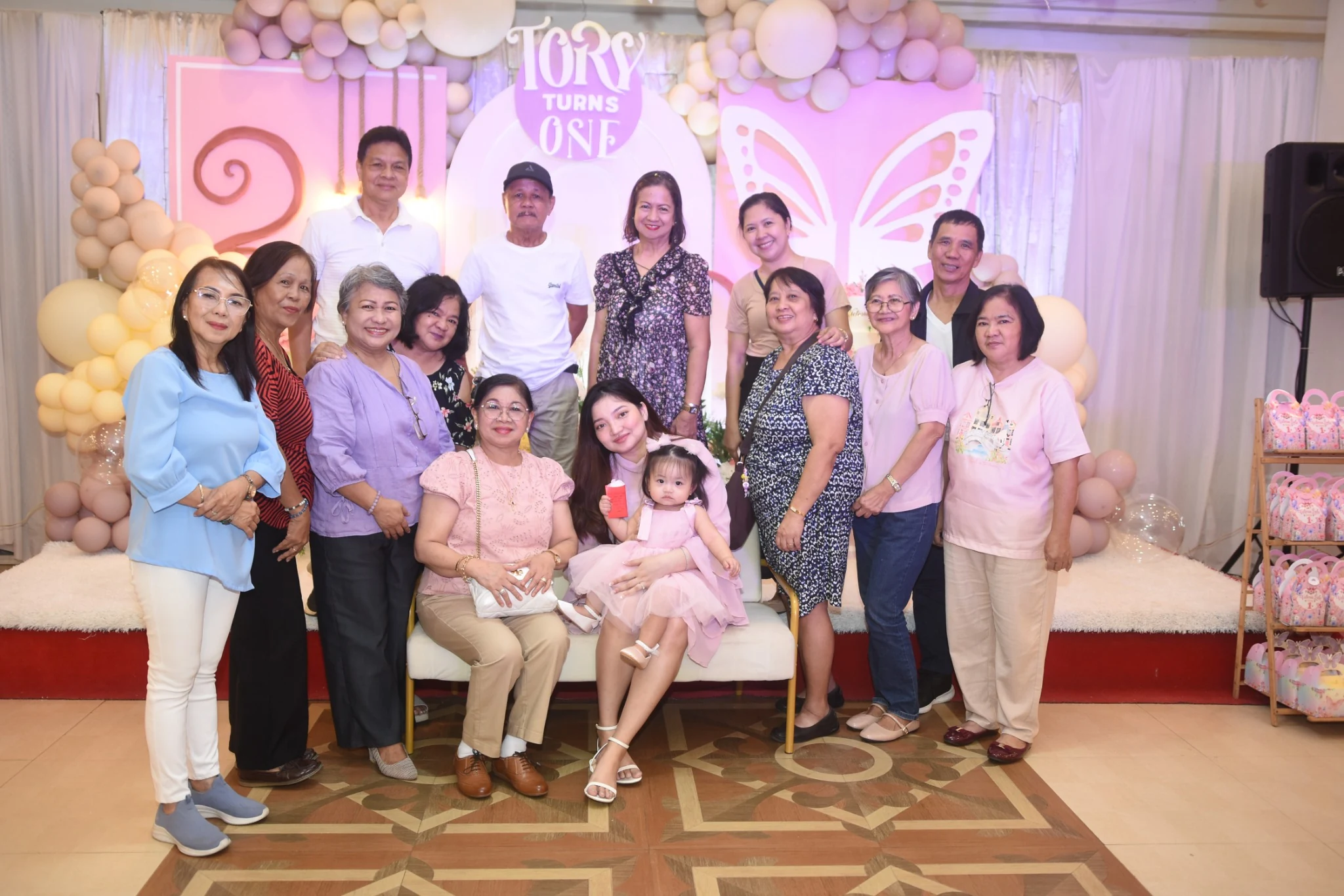 A large group poses around the seated birthday child beneath the Tory Turns One sign.