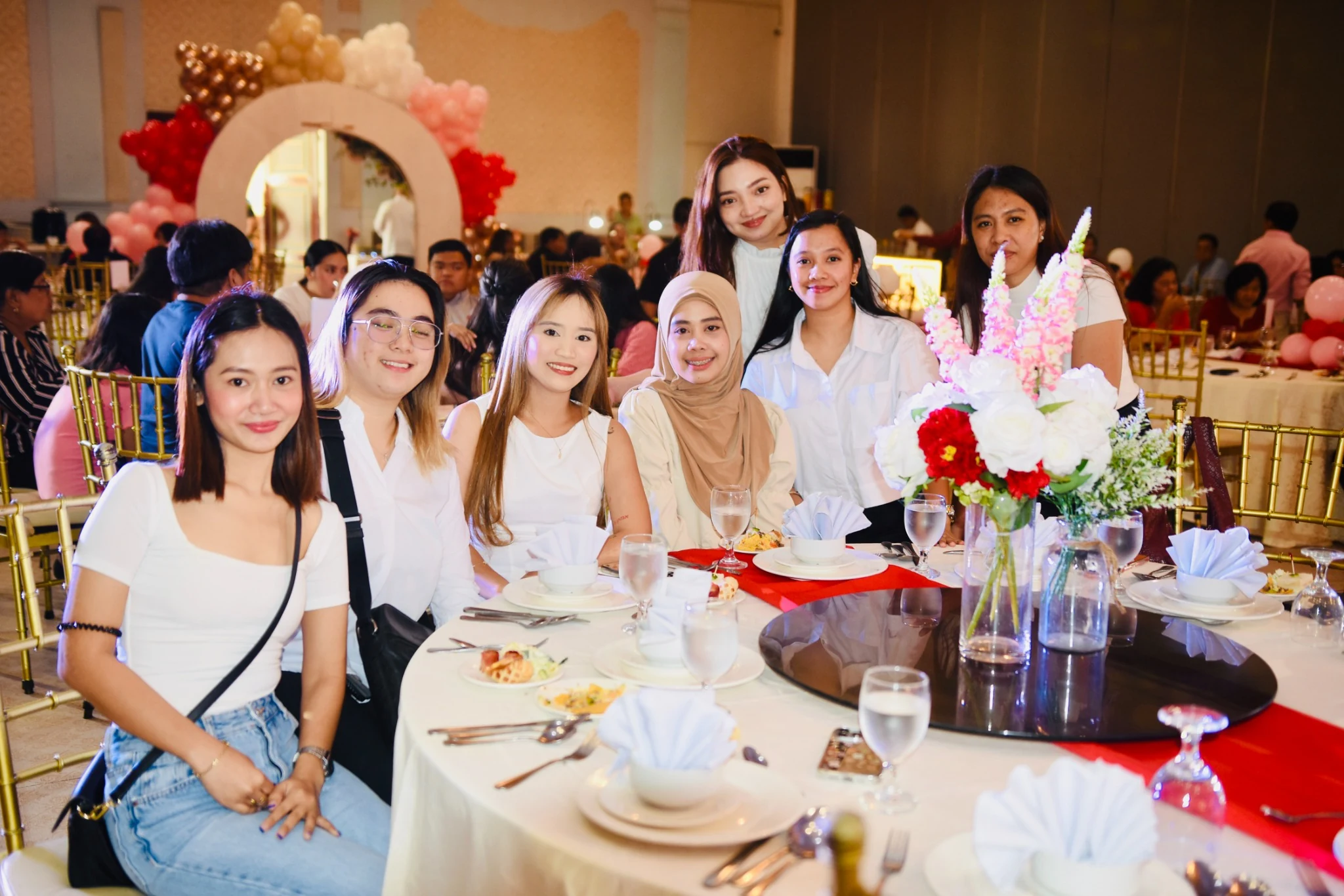 Guests pose at a reception table beside a tall floral centerpiece.