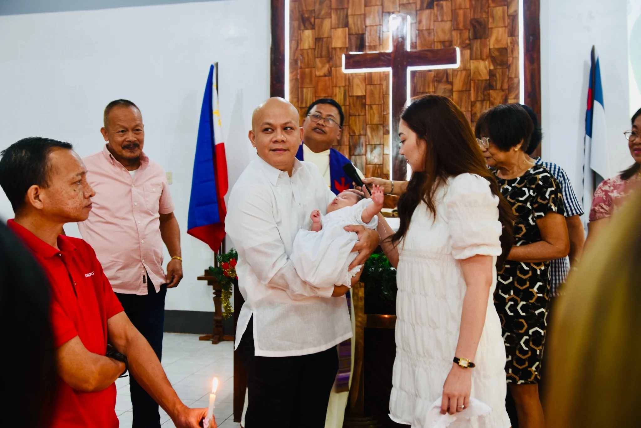 Adults gather around a baby in white during the church ceremony.
