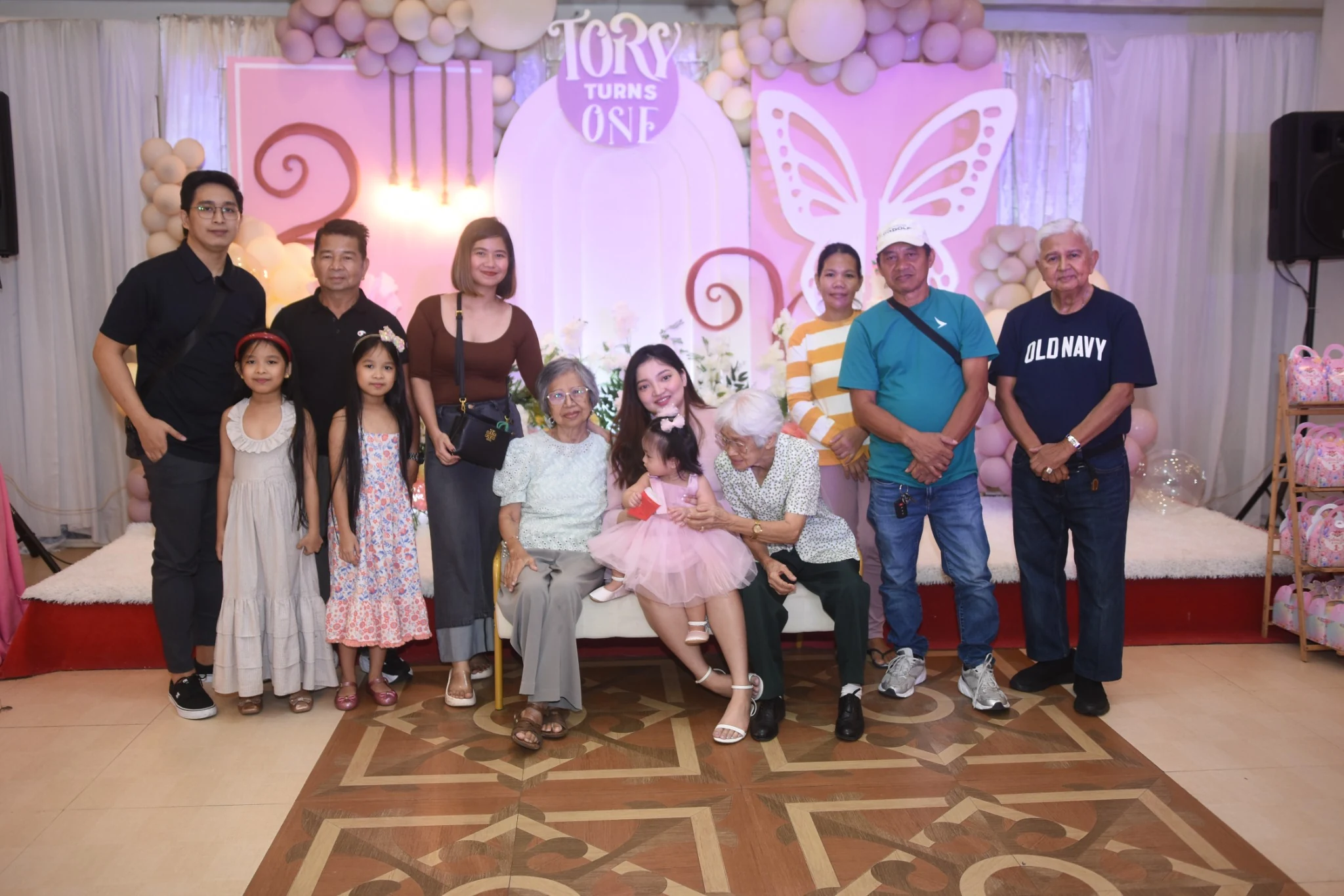 Guests gather for a group photo as a seated guest leans toward the birthday child.