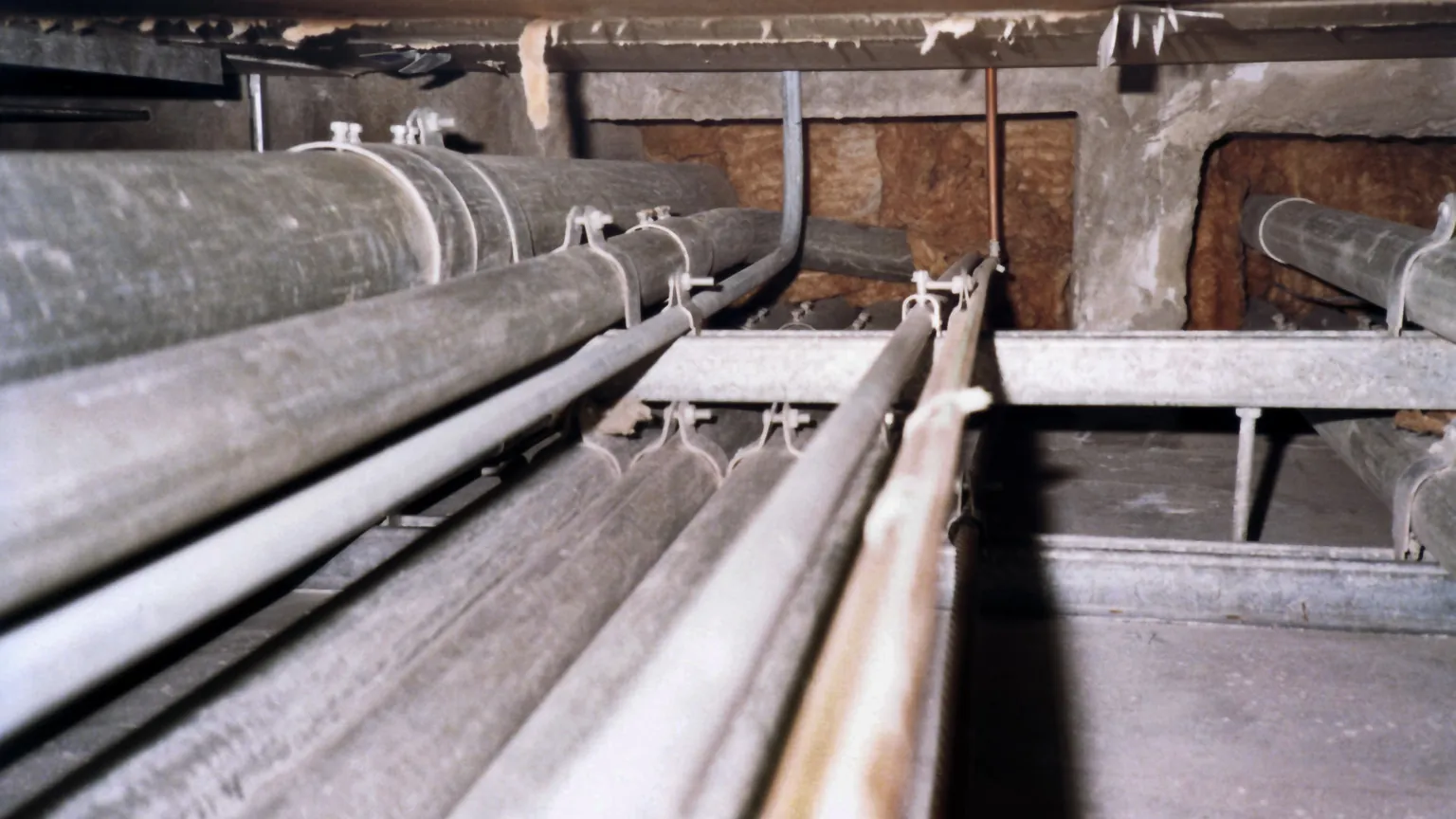 Metal electrical conduits run above an open ceiling and pass through an insulated wall.