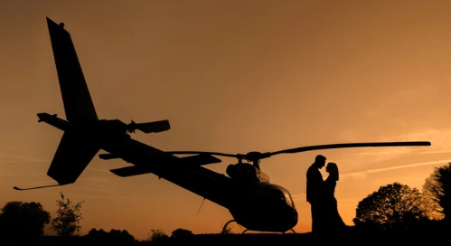 Couple silhouette at sunset with helicopter