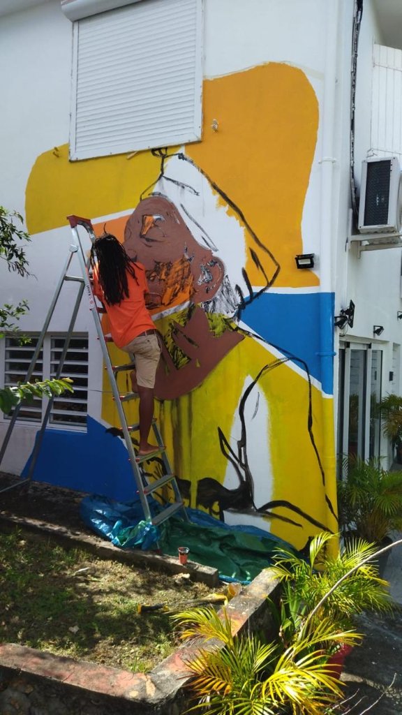 Artiste sur échelle peignant une fresque abstraite en jaune et bleu