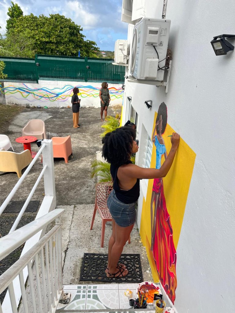 Artiste peignant une silhouette féminine sur le mur extérieur de Kréya'Kaz