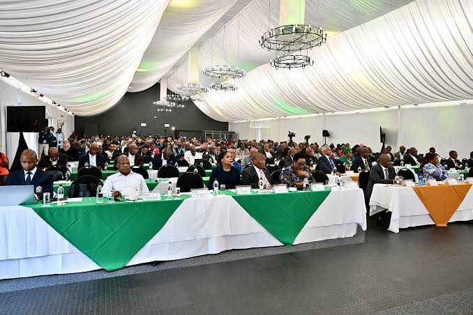 Delegates seated at green and white draped conference tables in a large hall with chandeliers