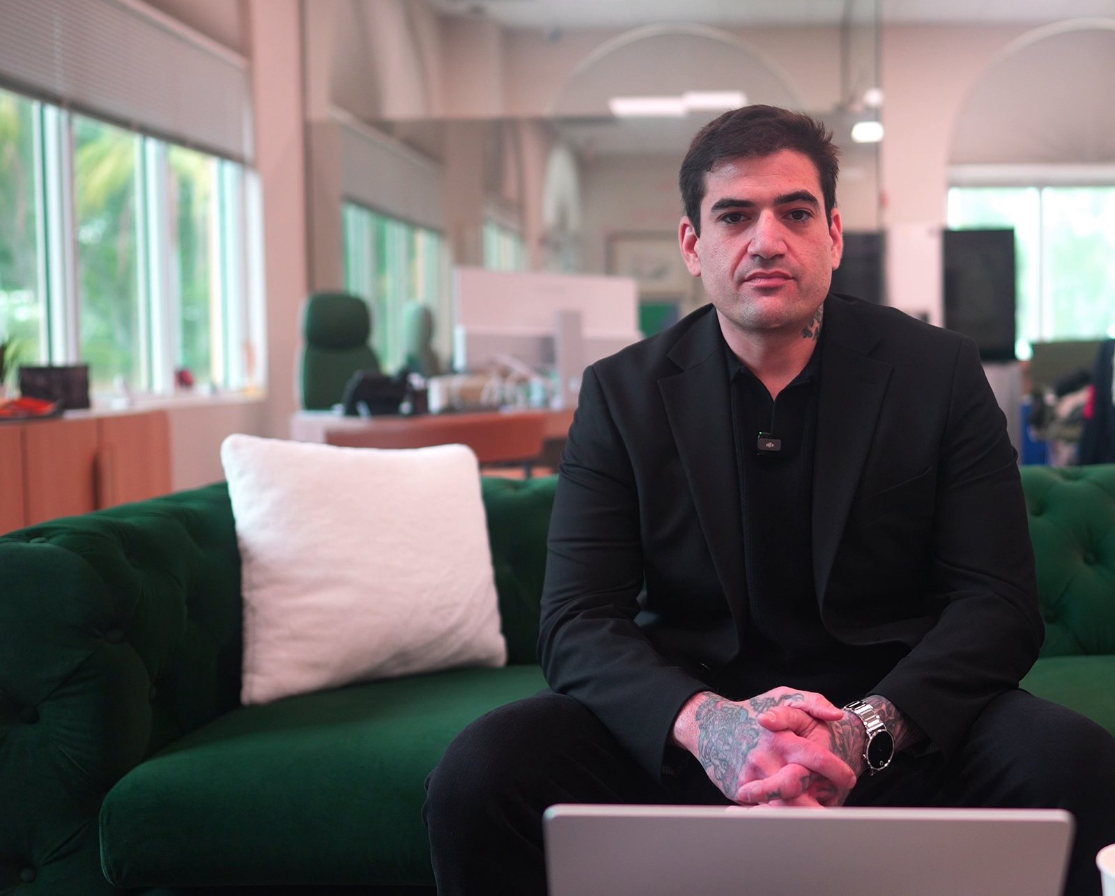 Sam Kaye seated on a green couch in an office, mid-conversation
