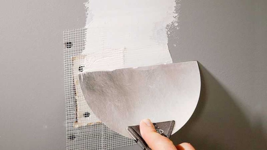 Drywall patch being skimmed with a knife