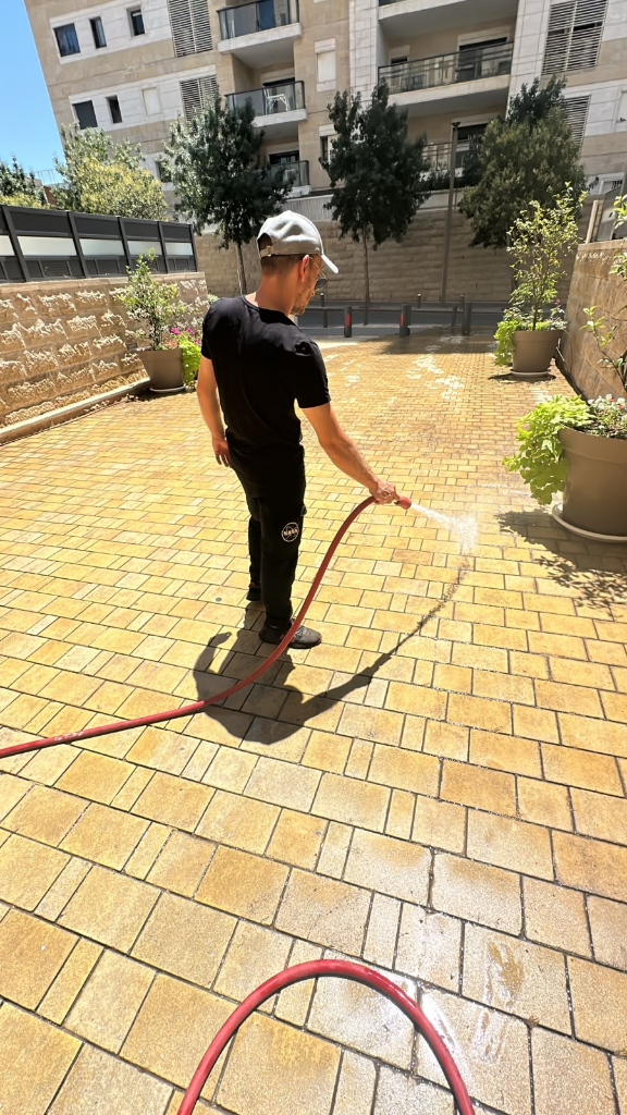 עובד מנקה בלחץ מים שביל מרוצף בבניין מגורים
