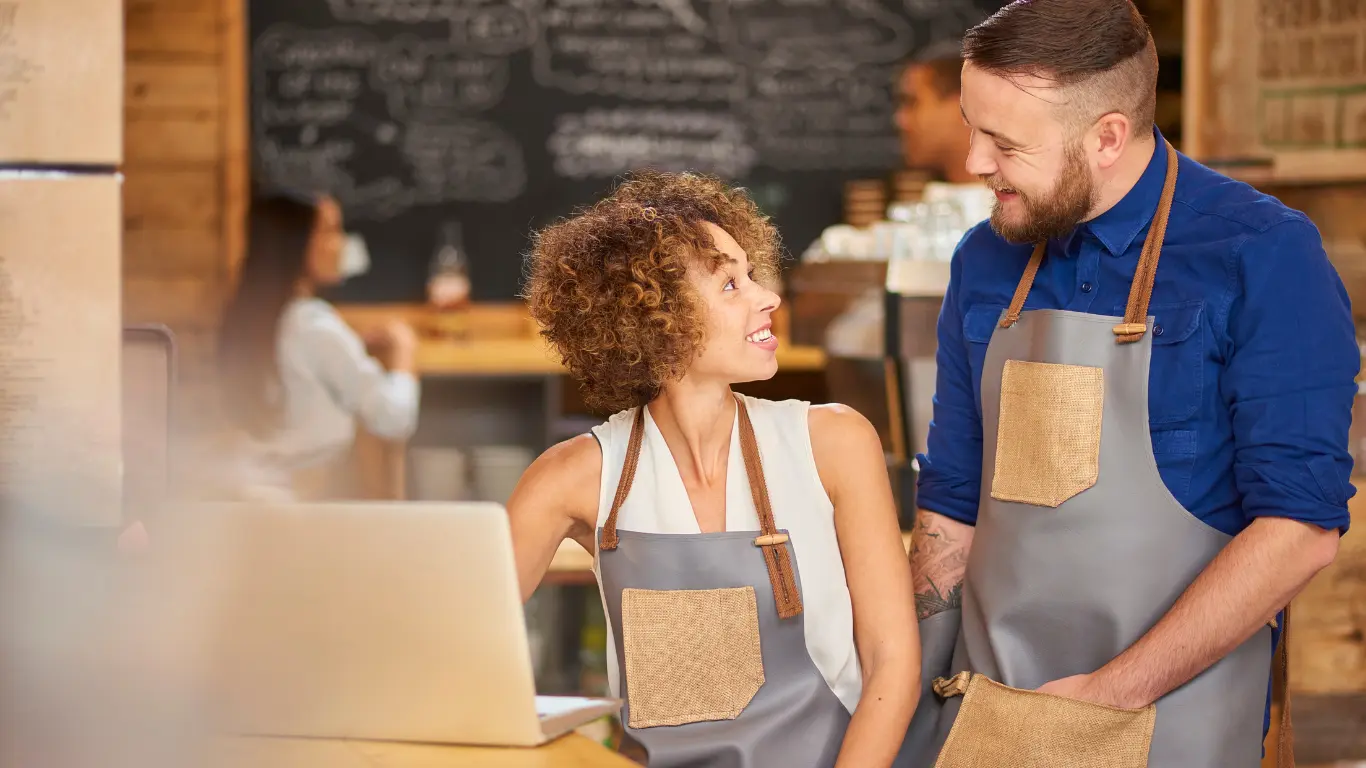 Small business owners in aprons reviewing their website together at a cafe