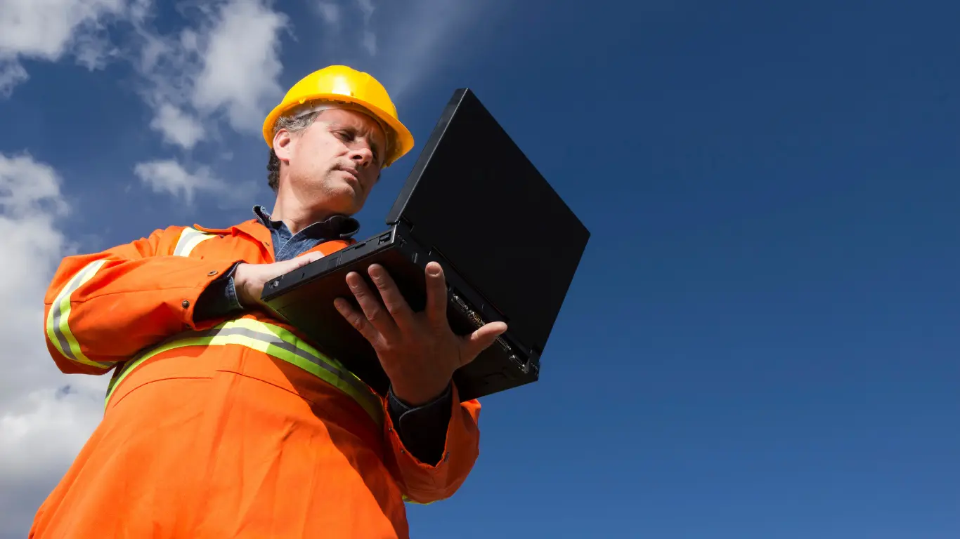 Contractor in safety gear using a laptop outdoors