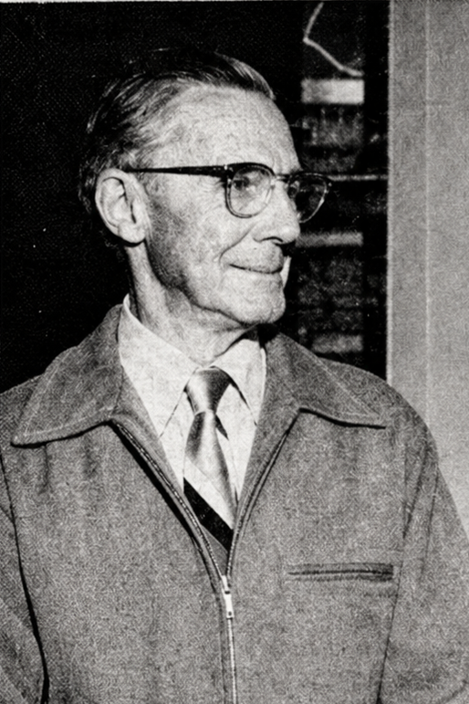 Charles Gierse in later life, in profile: grey hair combed back, thick-rimmed glasses, light collared shirt, striped tie and a zip-front jacket.