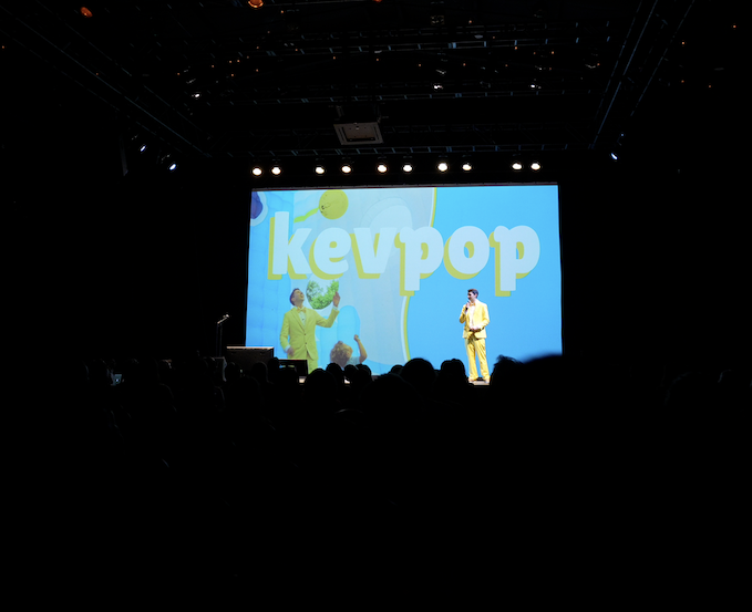 KEVPOP in a yellow suit holding a microphone on a stage