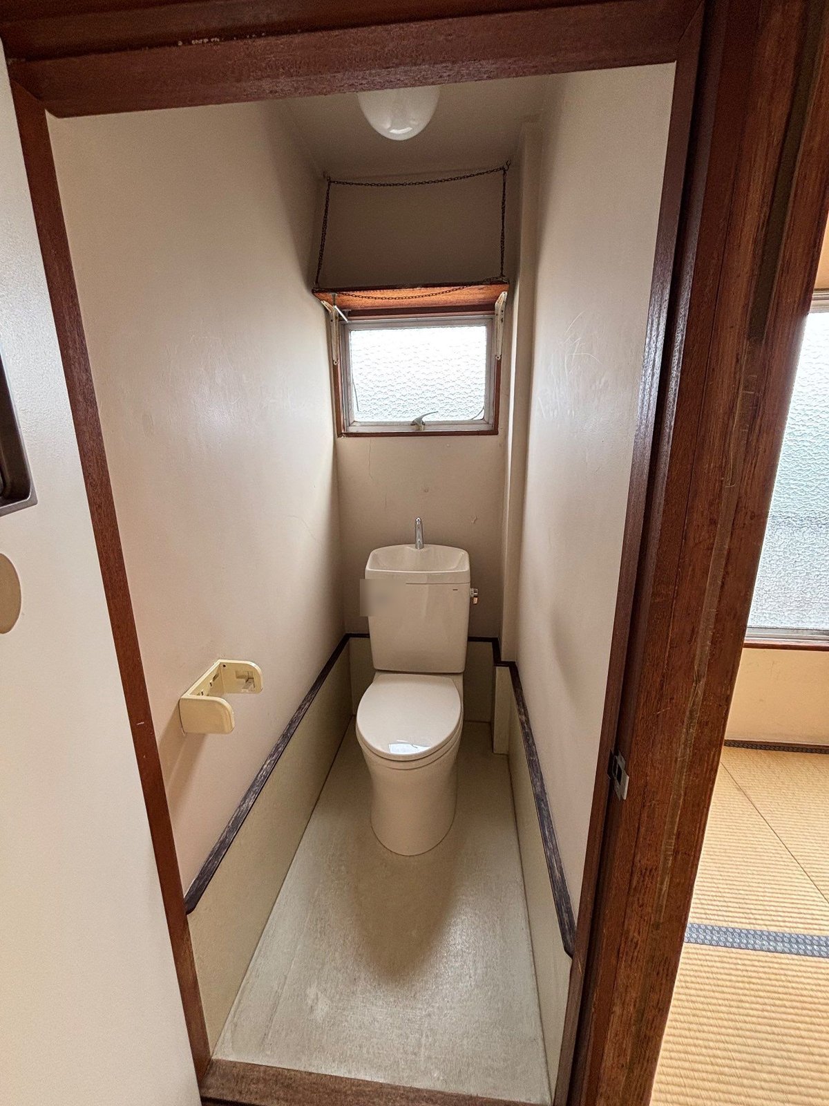 家財の片付けを終えた集合住宅のトイレ。床には何も残っておらず、奥に小窓、右手に和室の畳が見える
