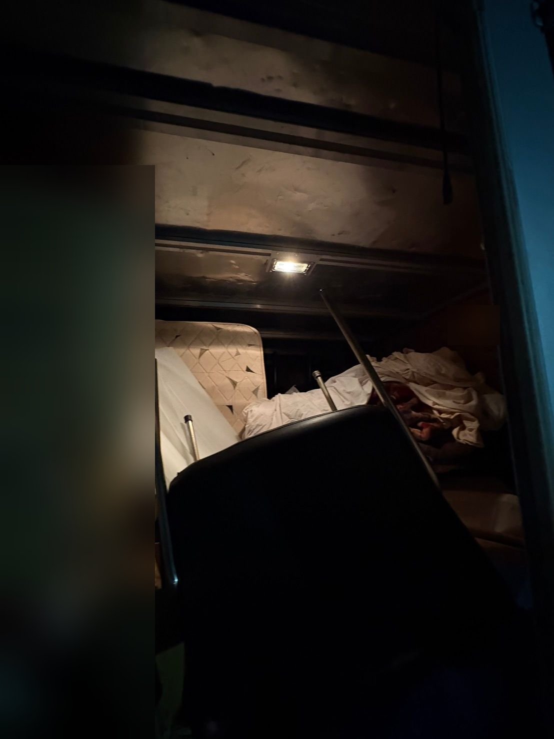 照明をつけたトラックの荷台。奥にマットレスと白い布団やシーツ類、手前に黒いソファのような家具が積まれている