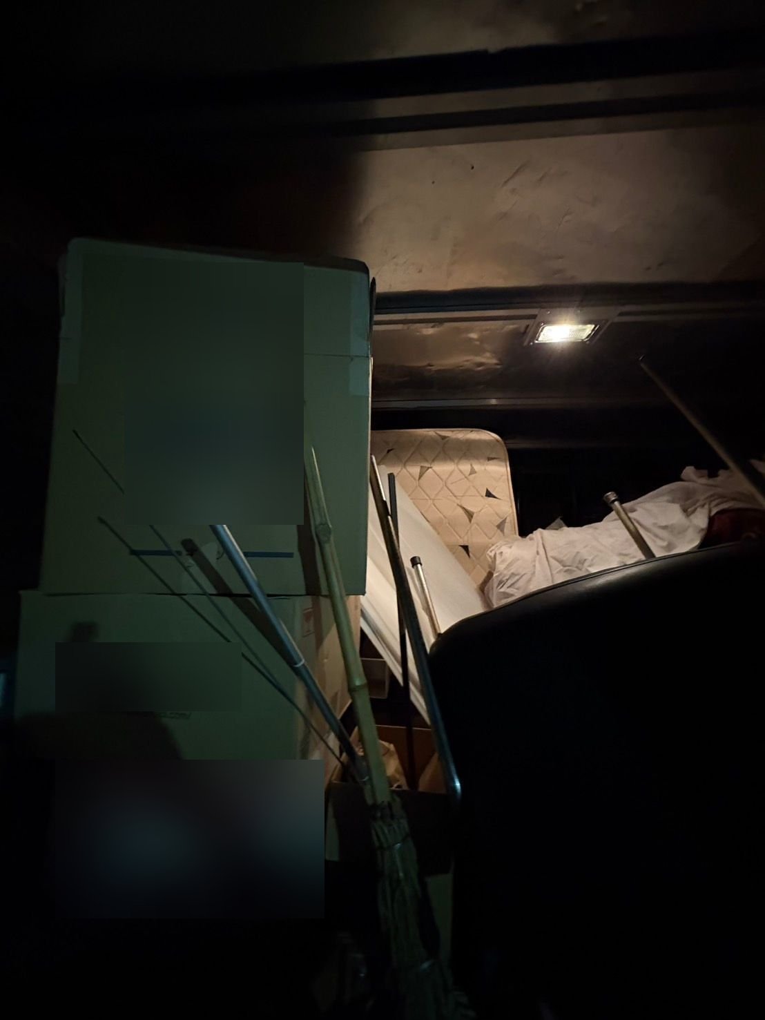 トラックの荷台。積み重ねた段ボール箱の手前に竹の棒やほうきがあり、奥にマットレスと布団が見える