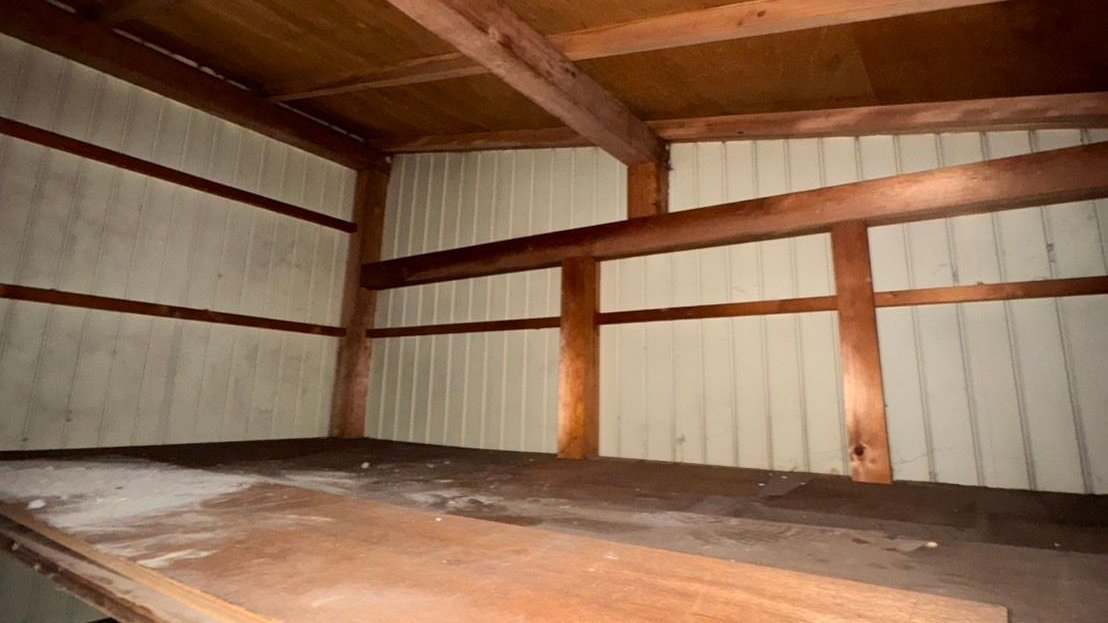家財を運び出した後の物置の中。板張りの棚と波板の壁が見え、棚の上には何も残っていない