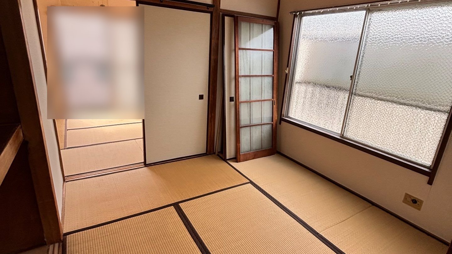 家財を運び出した後の集合住宅の和室。畳の上には何も残っておらず、右手に型板ガラスの窓、奥に隣の部屋が続いている