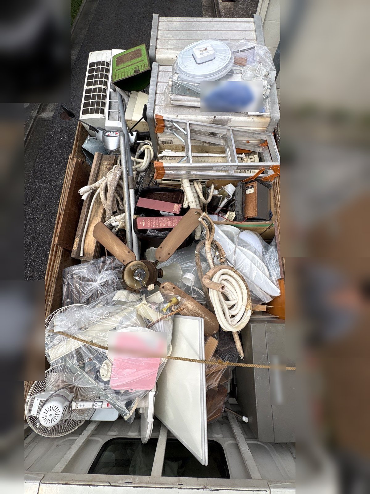 世田谷区の集合住宅から運び出した物を積んだトラックの荷台。扇風機、天井用の照明器具、エアコンの室内機とみられる機器、アルミの脚立、ホース類、金属製のケース、木の板などがロープで固定されている