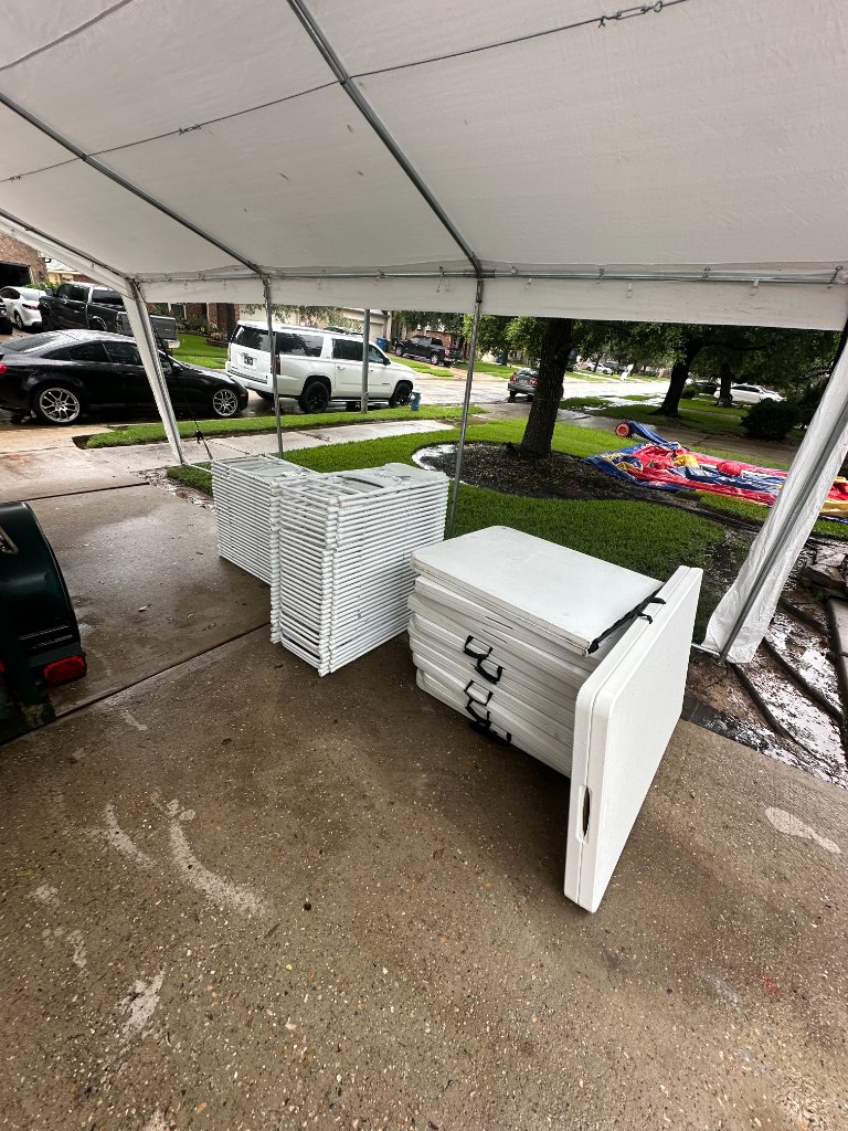 White tent on green lawn — stacked chairs & bounce house ready ⛺