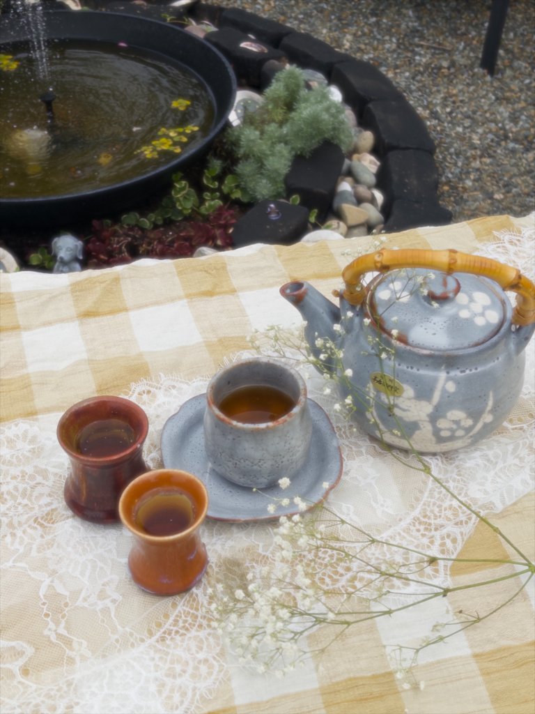 Handmade ceramic teapot and cups on a lace-covered picnic blanket