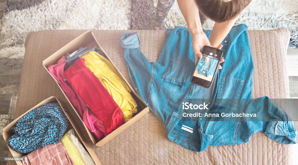Mains tenant un smartphone photographiant une chemise en jean posée à plat, cartons de vêtements à côté — illustration article comment faire de belles photos pour Vinted