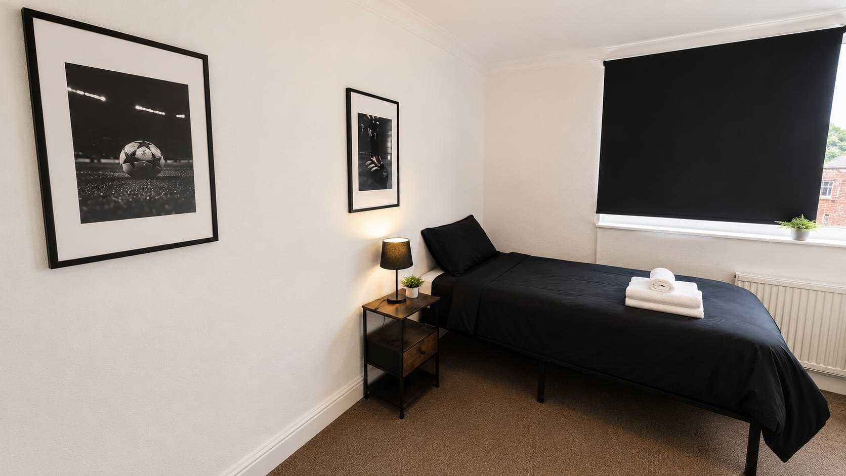 A modern single bedroom with black bedding, football wall art and a bedside lamp