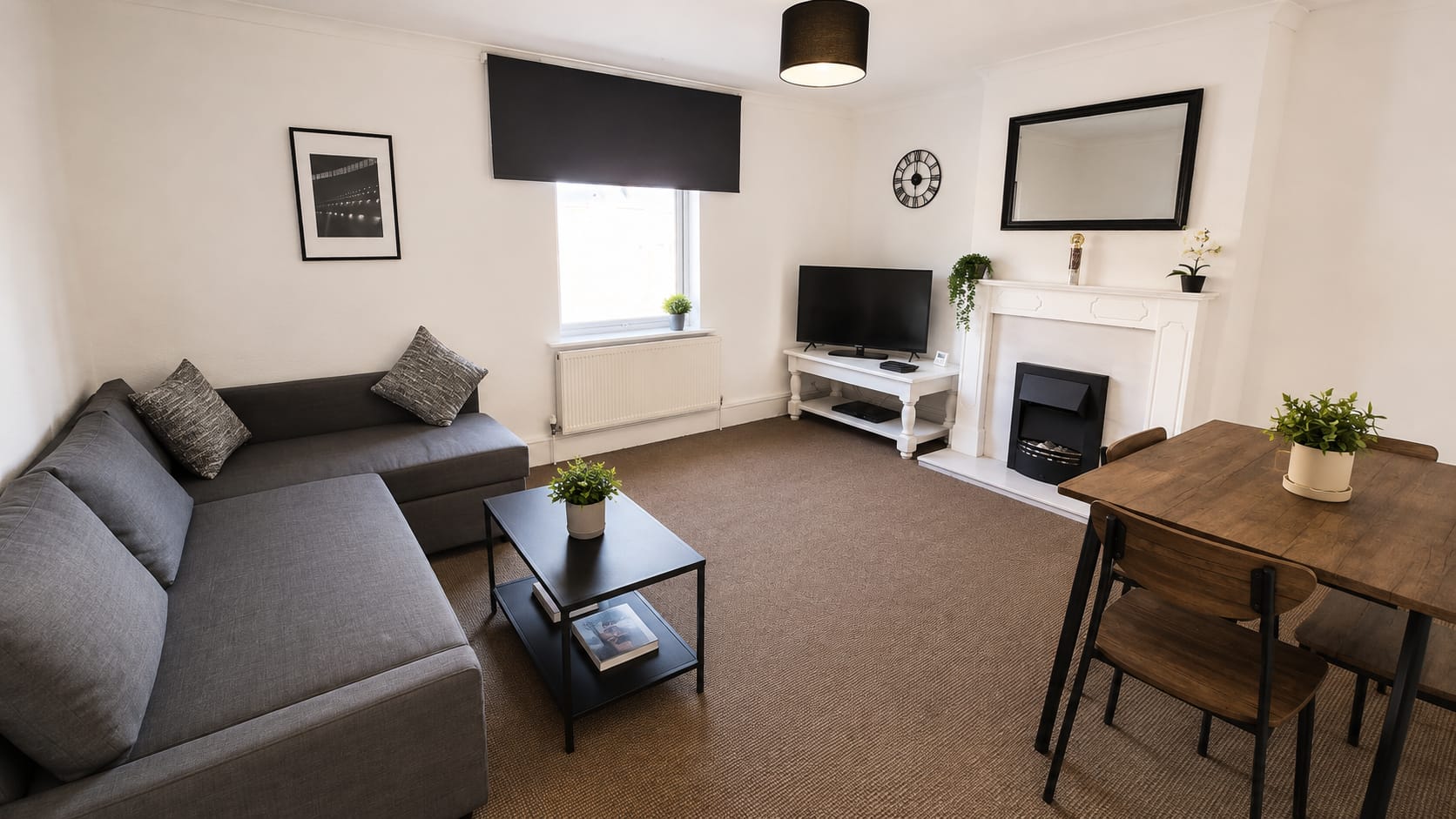 A bright modern shared lounge with grey sofa, dining table and football artwork