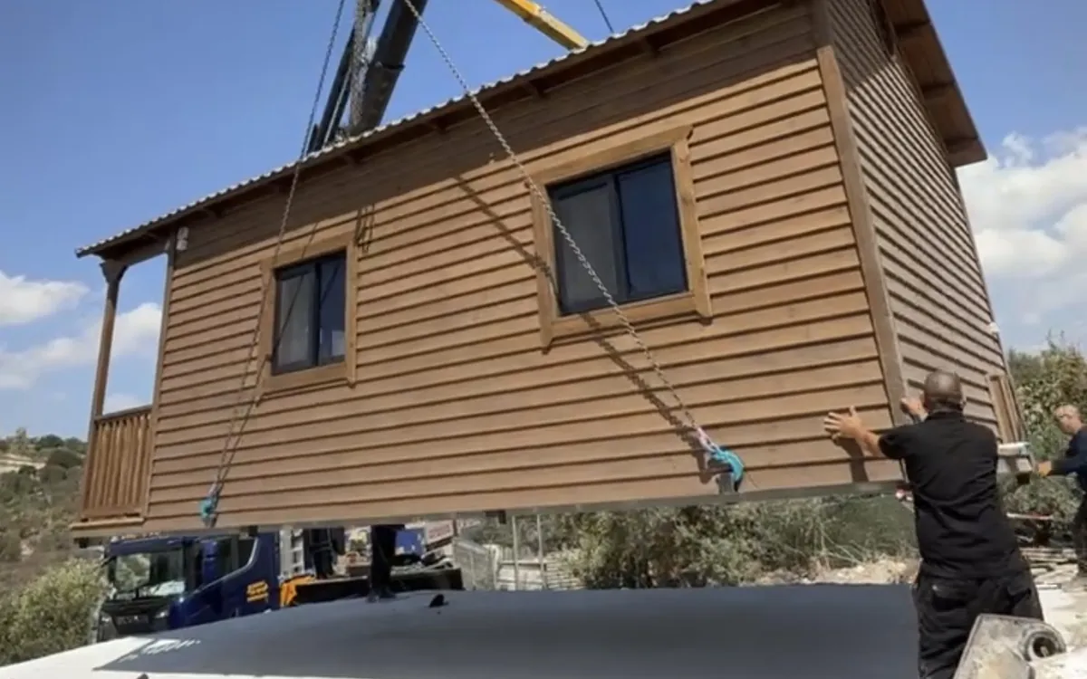 צימר מעץ מונף במנוף, וצוות מכוון אותו אל המקום שלו