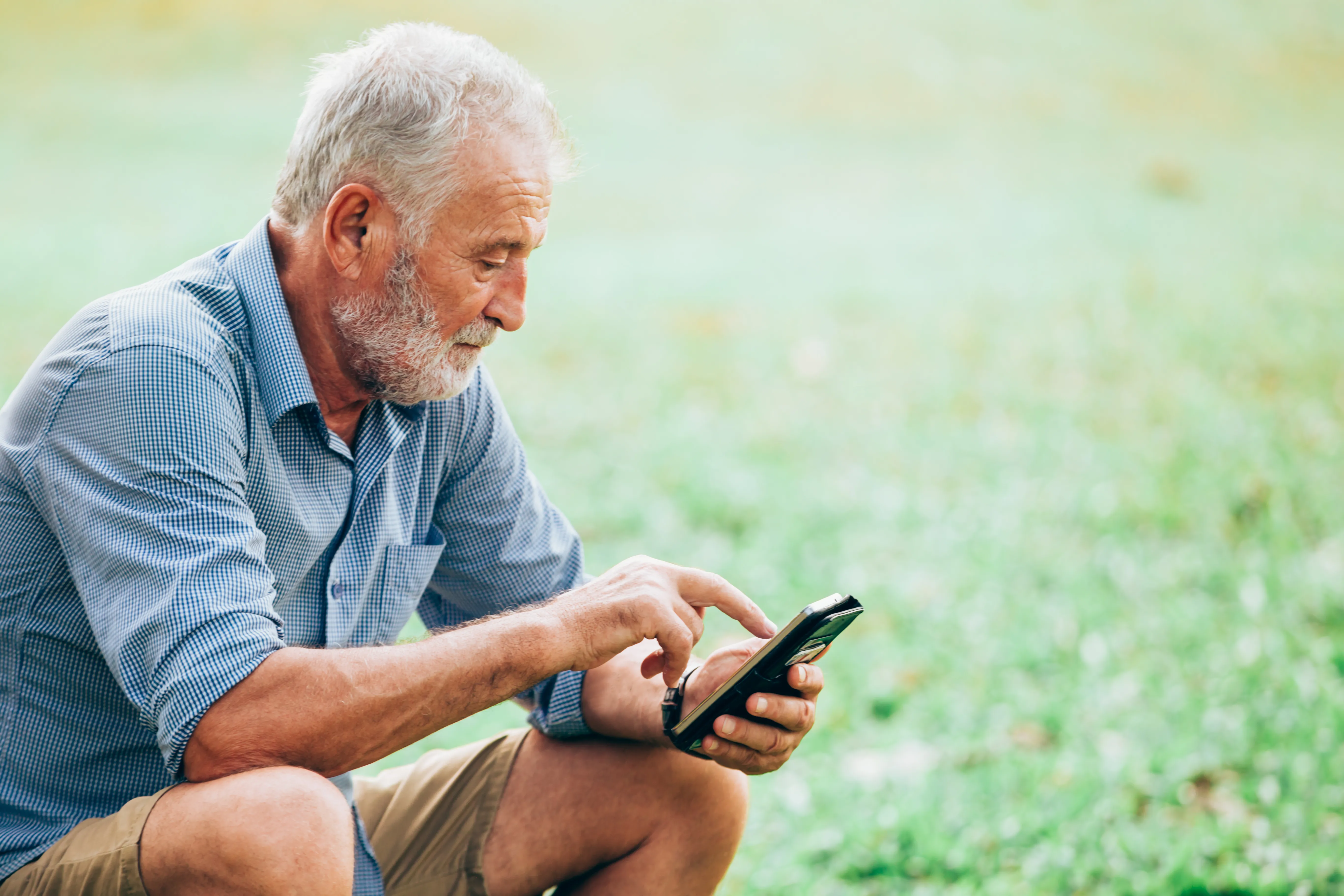 An older resident reading city news on his phone in the park