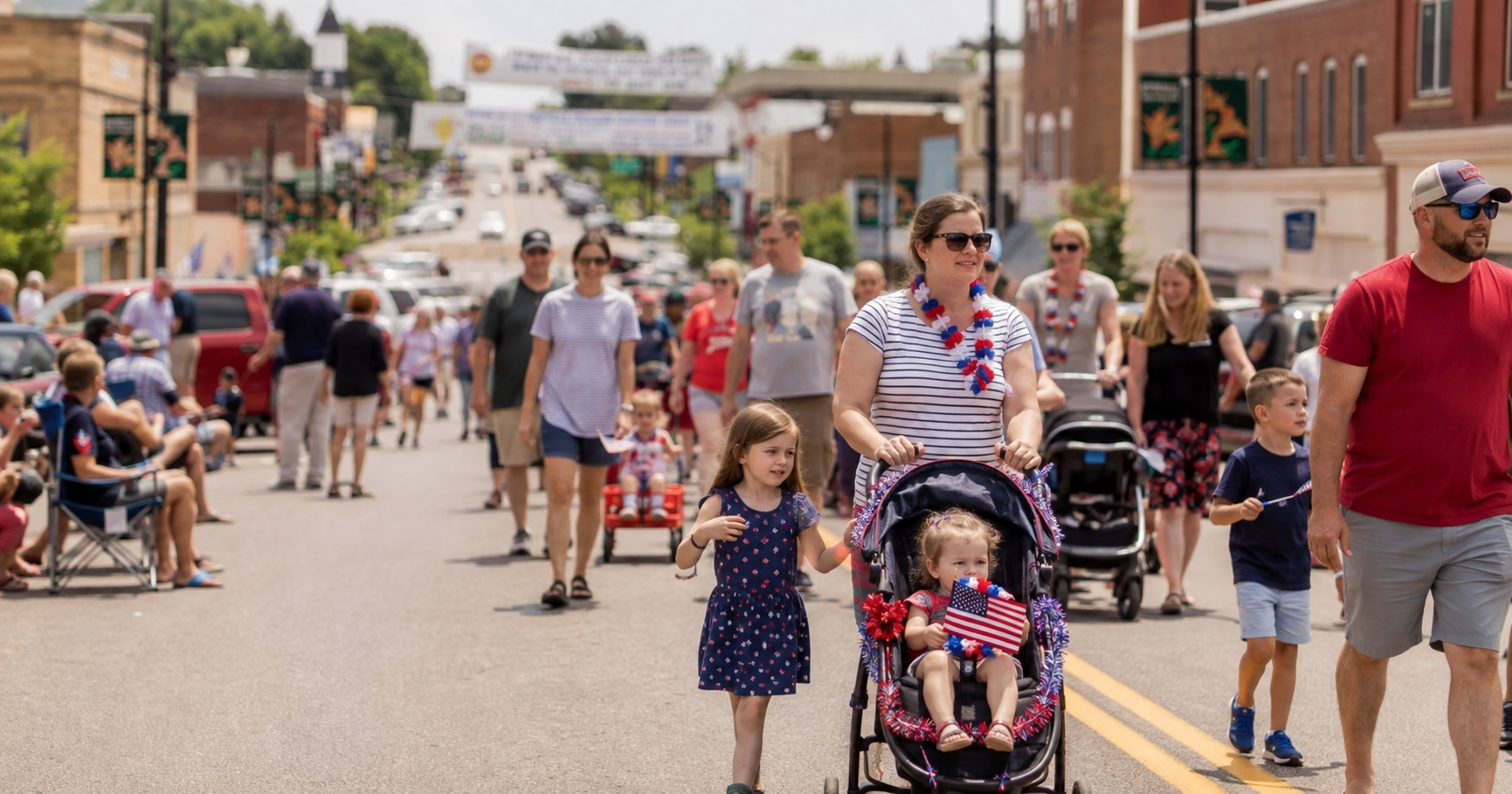 Families with strollers, flags and streamers walking down a small-town main street on parade day