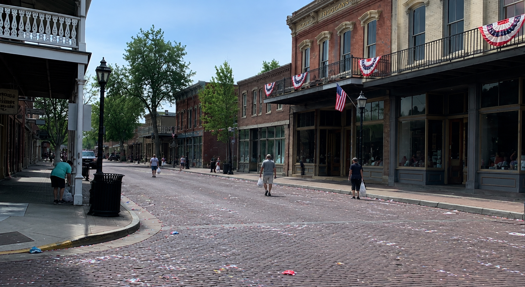 A main street still hung with bunting after a parade, confetti on the bricks and a crew starting cleanup