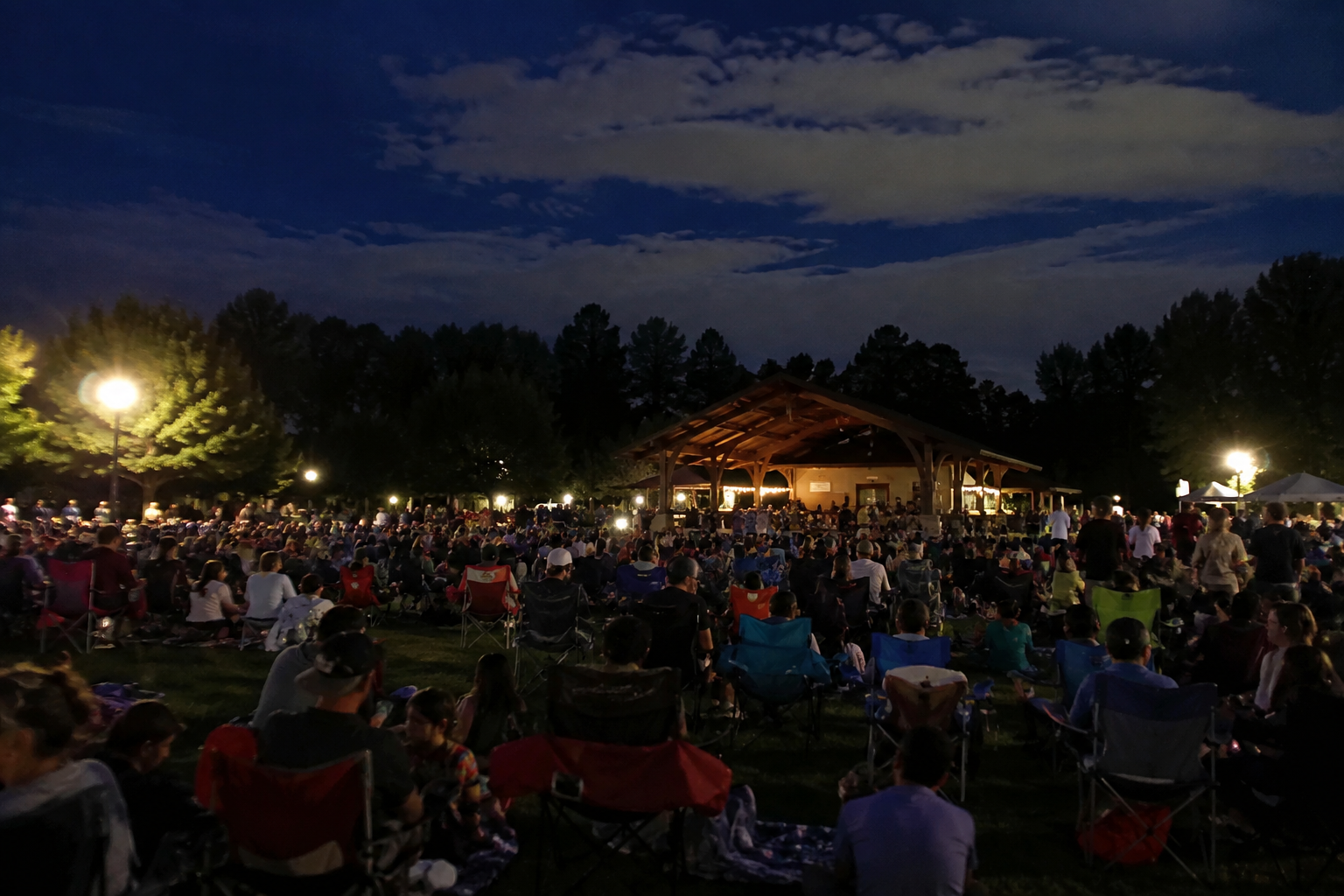 A crowd waiting in lawn chairs and on blankets after dark at a city park pavilion