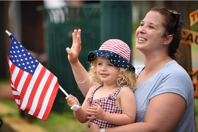 A mother and daughter waving a flag at a hometown parade