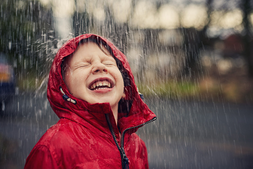 Child smiling in the rain wearing a red raincoat