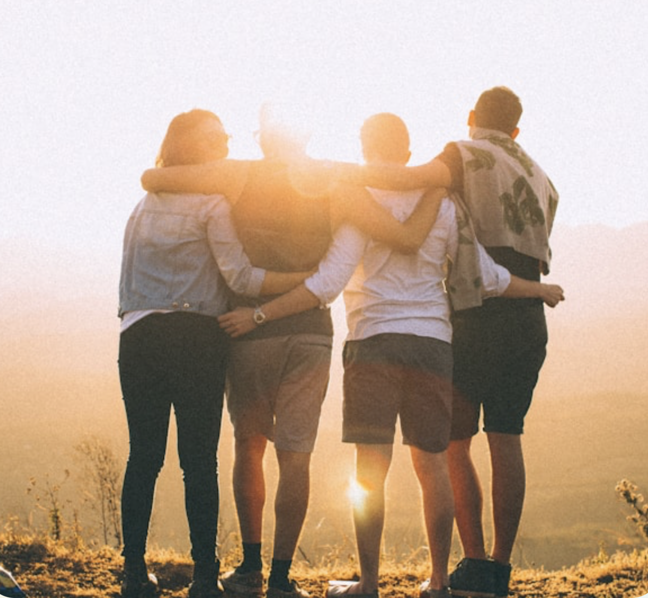 Four people standing together at sunrise, arms around each other's shoulders