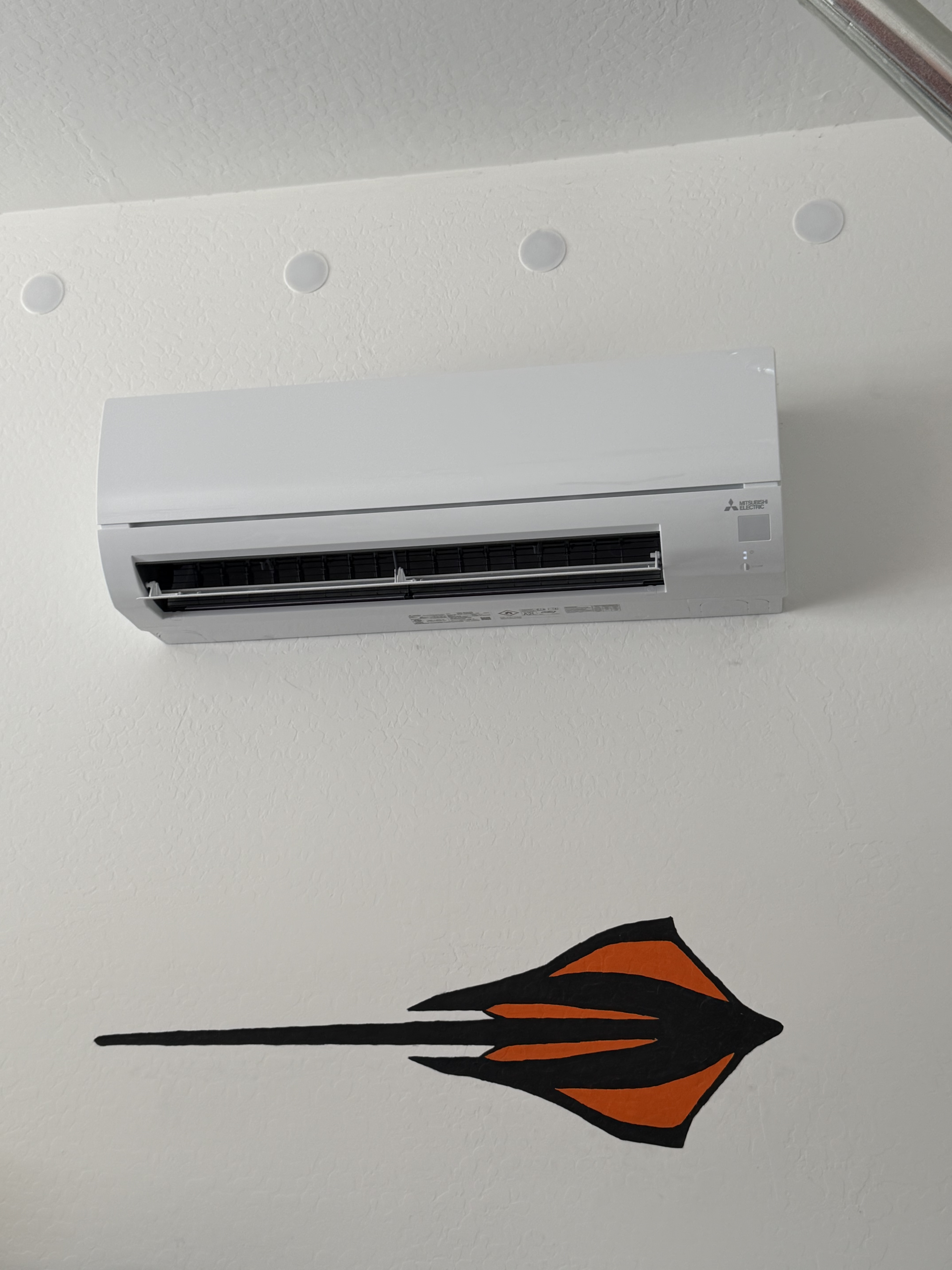 Indoor wall-mounted Mitsubishi Electric mini-split air handler installed on a white wall above a stylized stingray wall graphic.