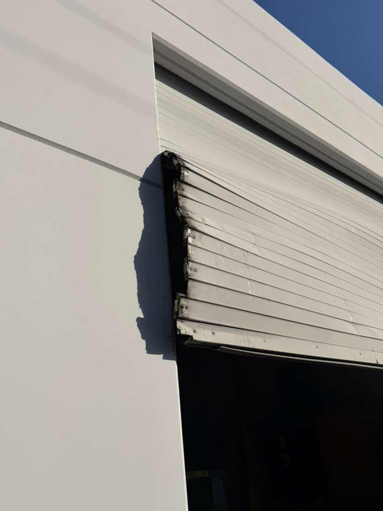 Roll-up door slat damage repair Commercial roll-up garage door slat damage close-up showing bent and misaligned panels before repair