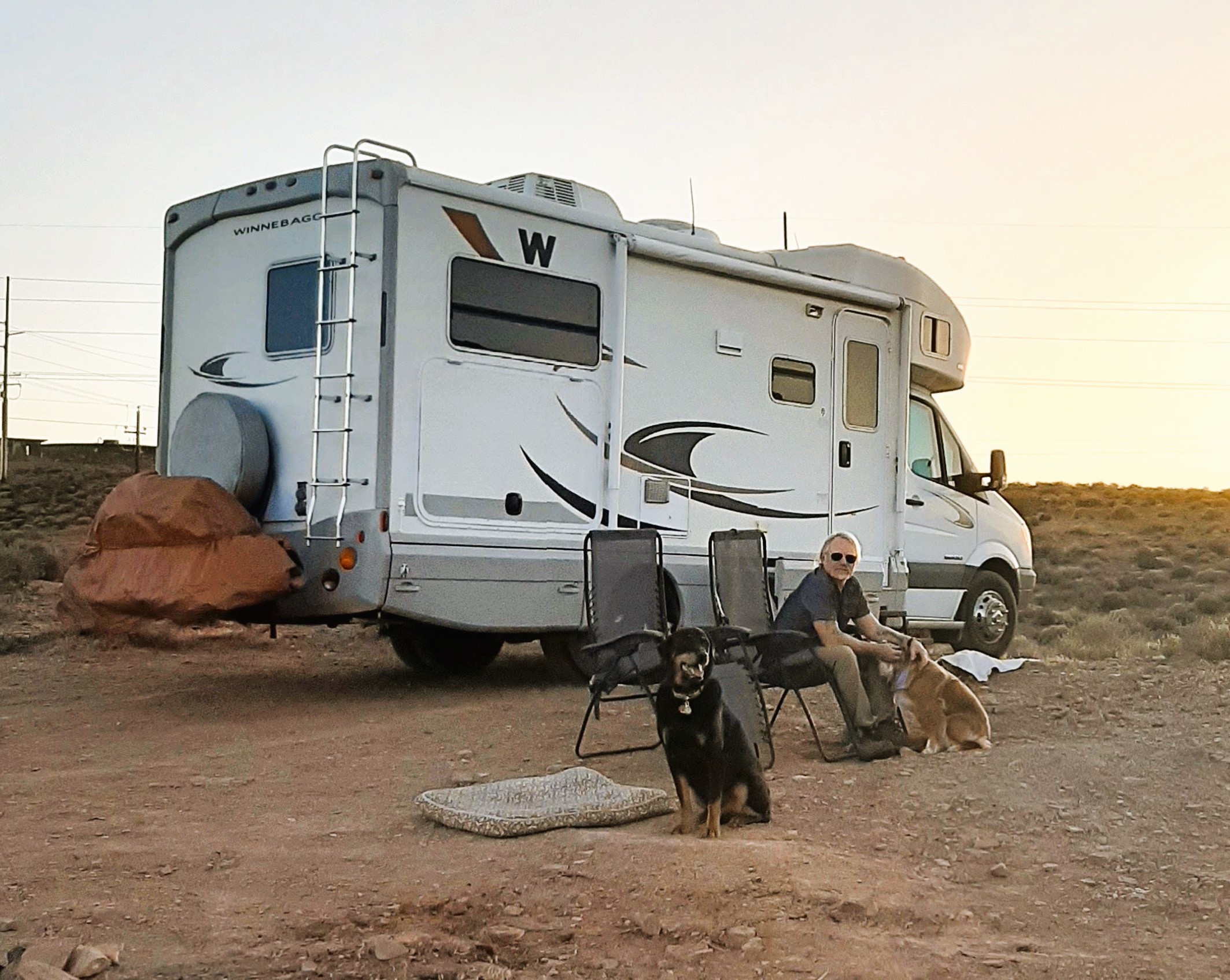 John sitting in a camp chair with two dogs at a desert campsite next to his Winnebago motorhome in Utah