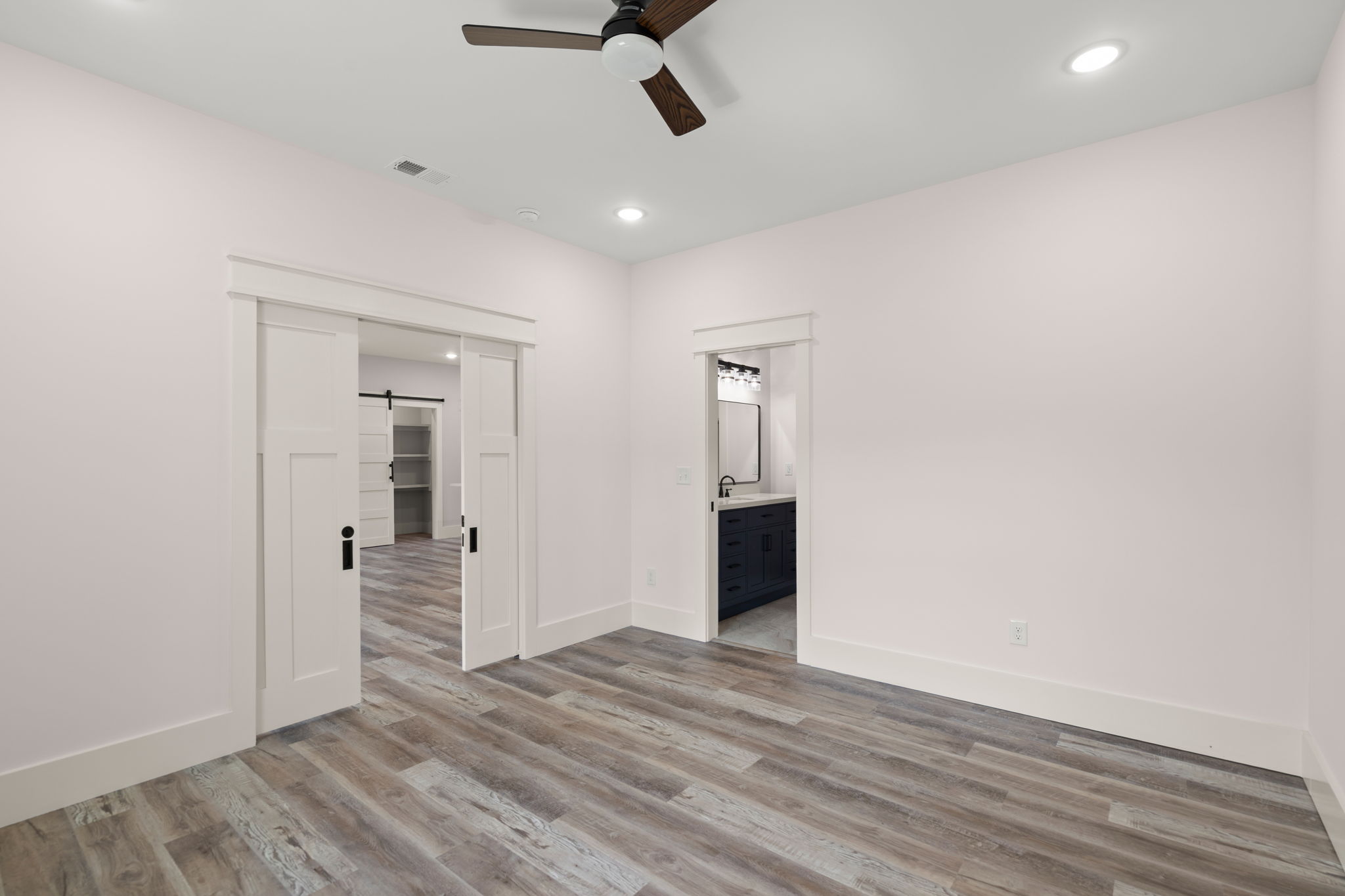 Bedroom with white barn doors open to a dark-floor room