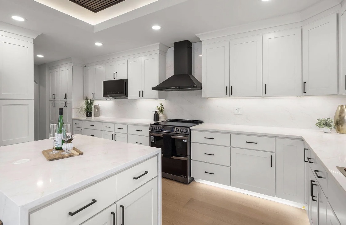 Kitchen with white cabinets, black appliances, and waterfall island