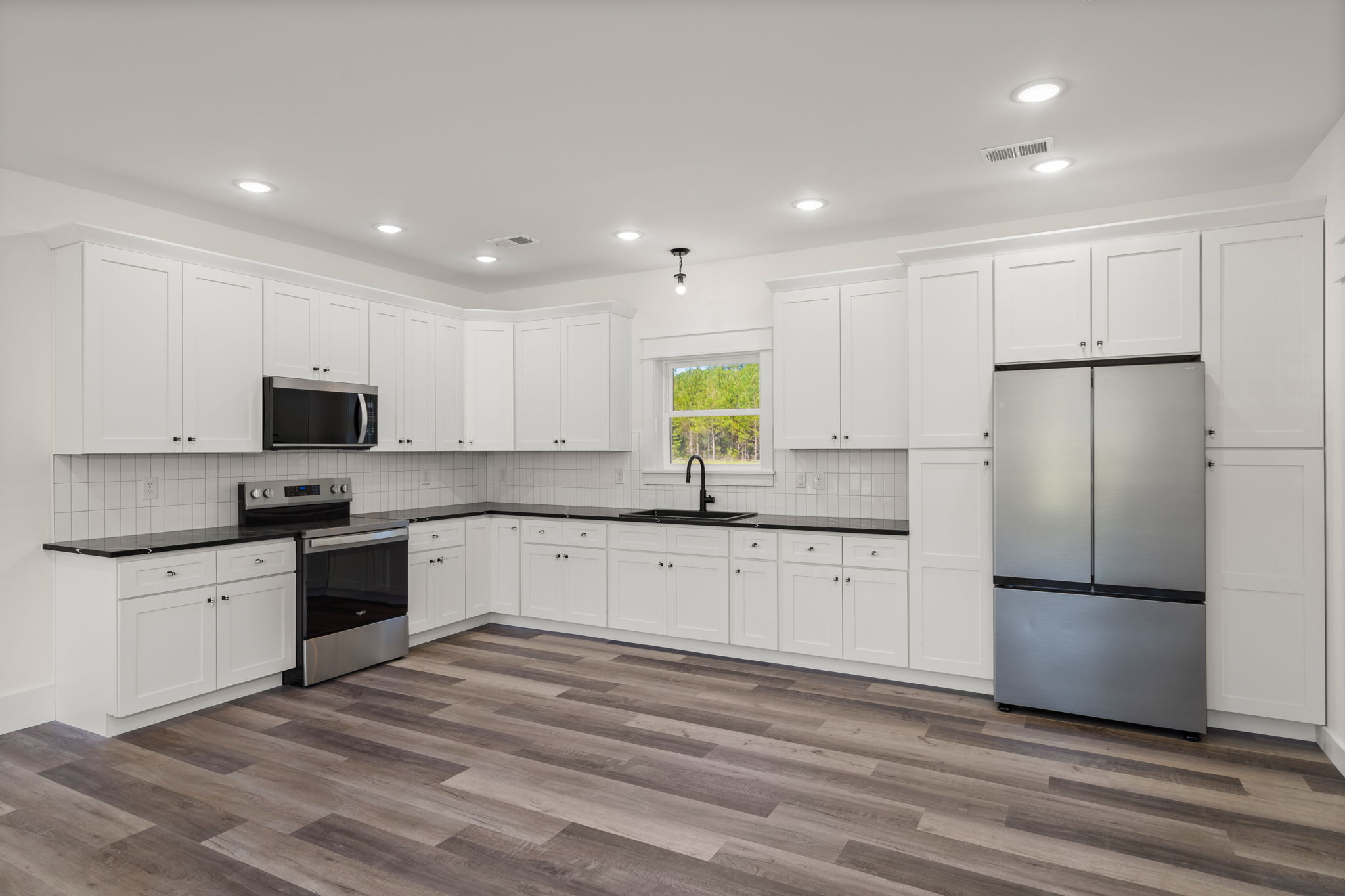 L-shaped kitchen with black quartz counters and stainless refrigerator