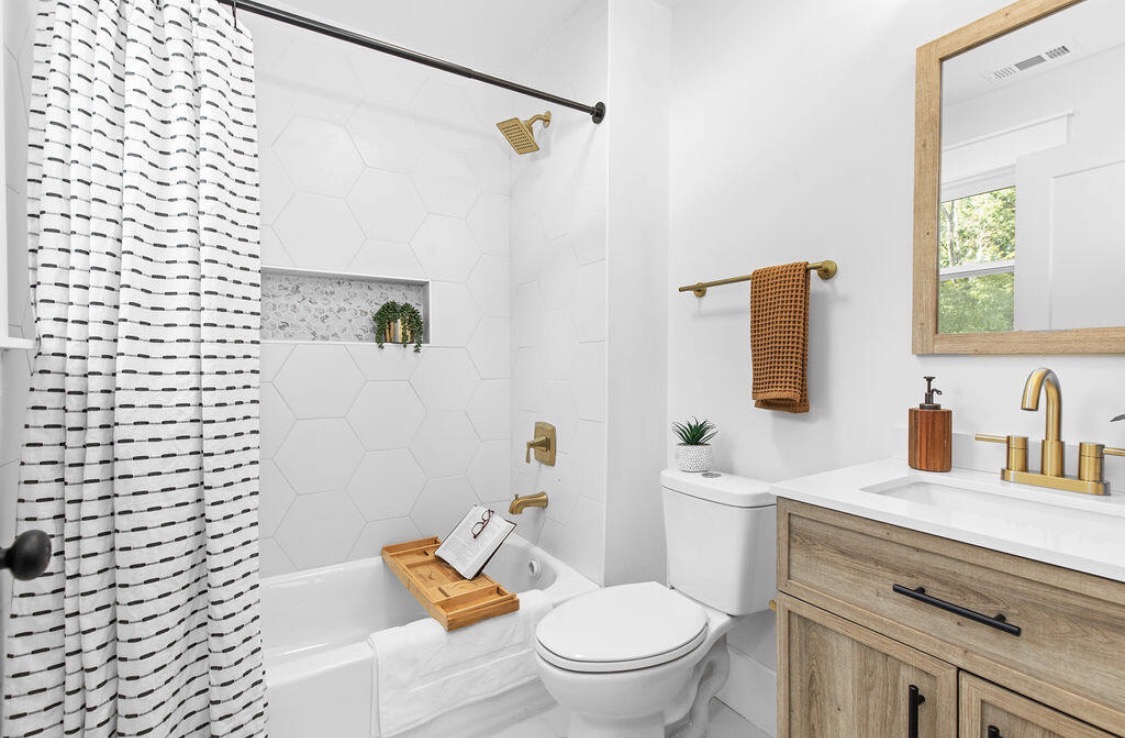 Bathroom with wood vanity, hexagon tile tub, and gold hardware