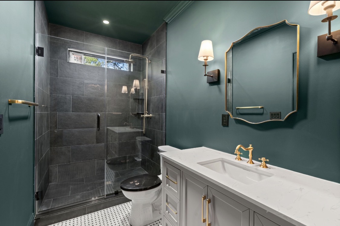 Teal bathroom with brass fixtures and gold-framed mirror