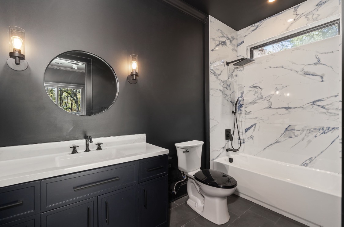 Bathroom with grey vanity, marble tub surround, and black fixtures