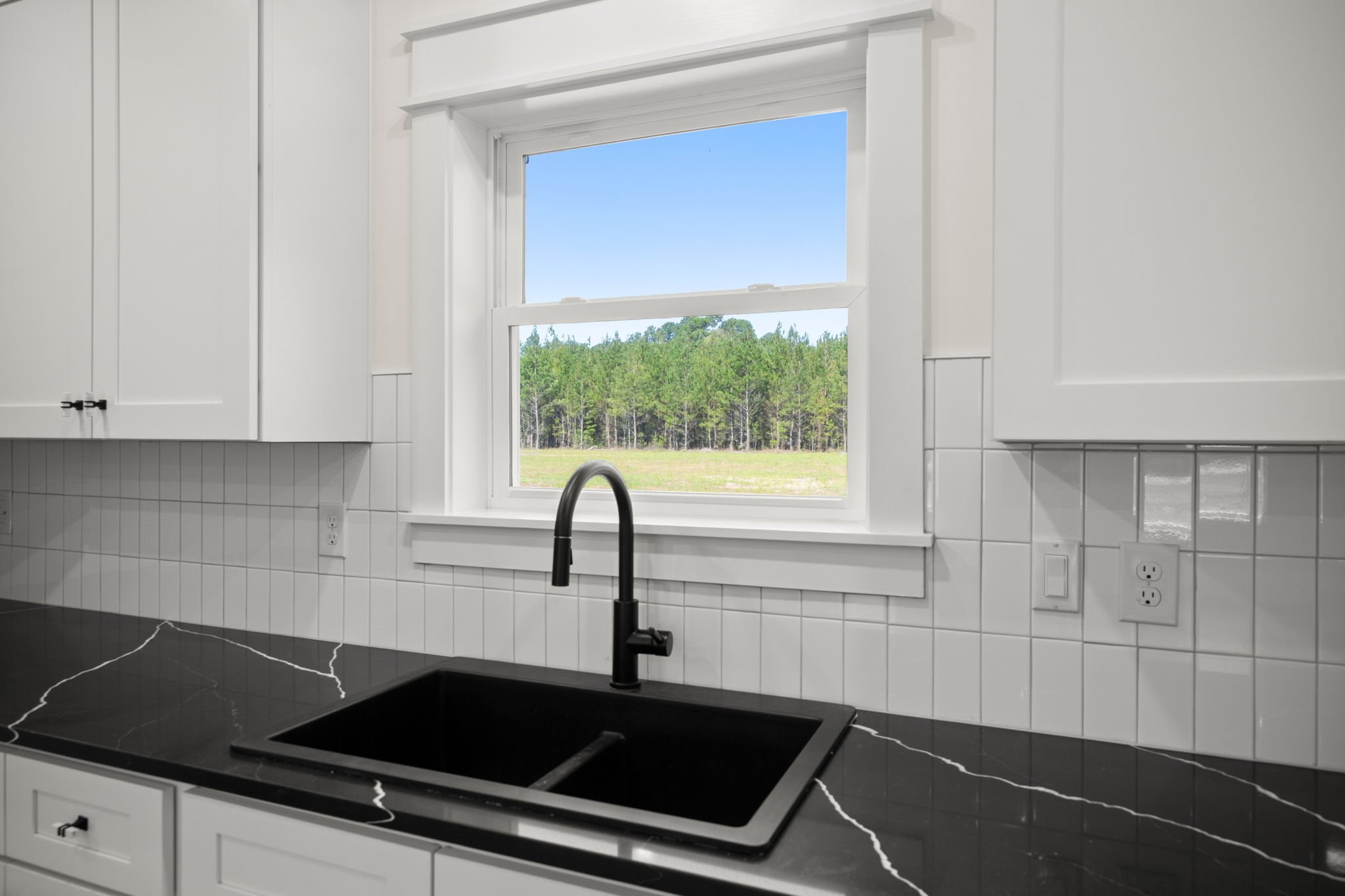 Black quartz sink counter with white subway tile and window views