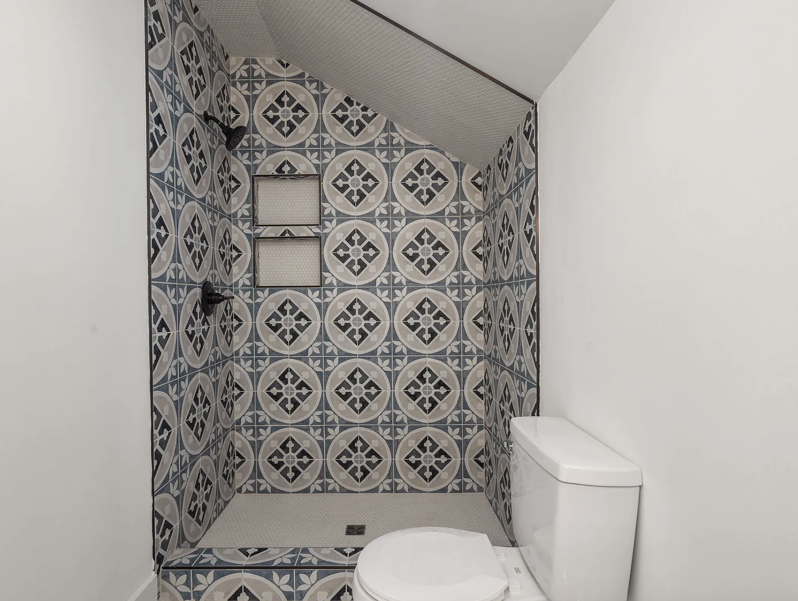 Shower stall with geometric tile under sloped ceiling