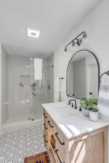 Bathroom with wood vanity, arched mirror, and herringbone shower tile